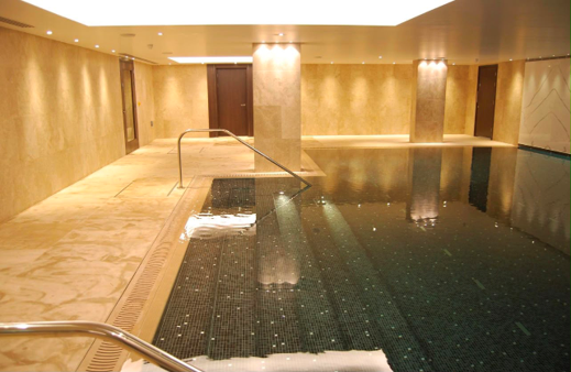 Indoor swimming pool with dark mosaic tiles, stone surround and stainless steel handrails