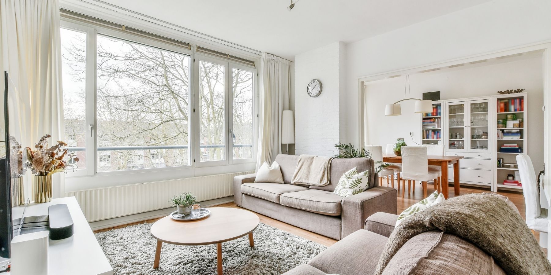 Bright open-plan living and dining room with large windows, sofas and built-in storage