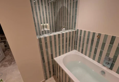 Completed Notting Hill bathroom with fitted bath, green and white striped tiles and recessed shower area