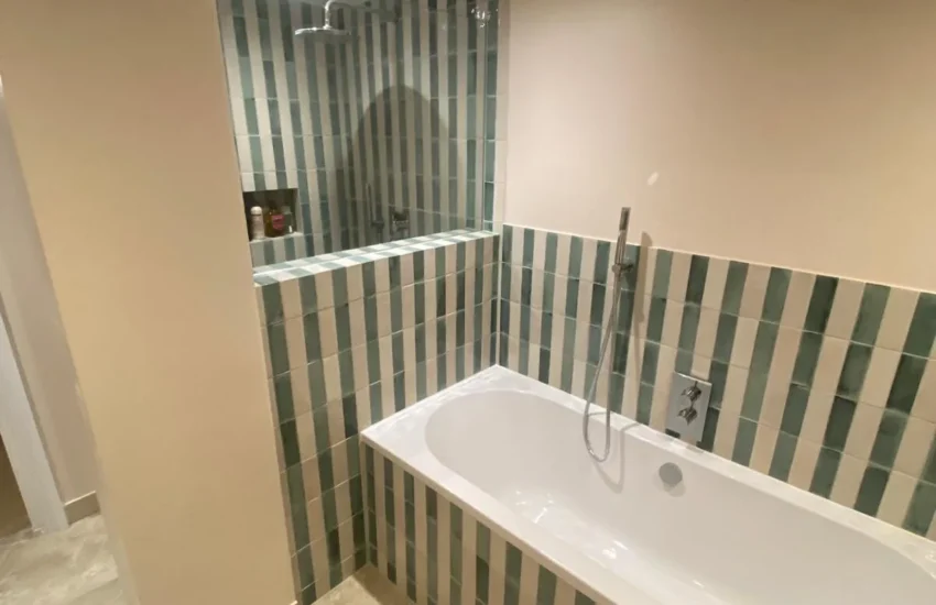 Renovated bathroom with fitted bath and green and white striped wall tiles in Notting Hill