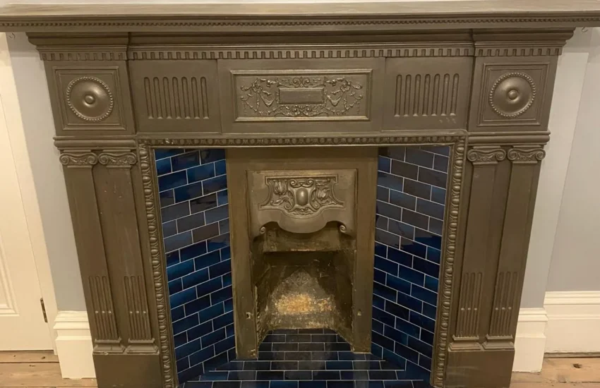 Ornate cast-iron period fireplace with blue tiled surround and hearth on timber flooring