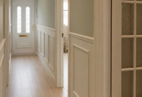 Refurbished hallway with decorative wall panelling, light wood flooring, white doors and recessed lighting