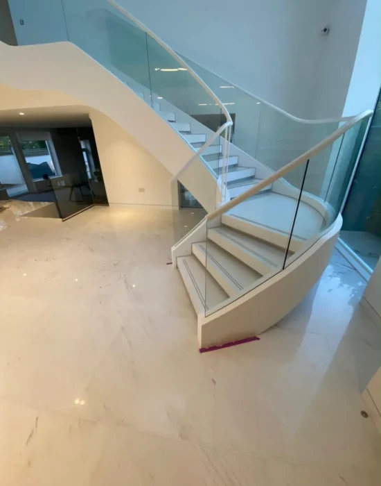 Finished bespoke curved staircase with glass balustrade, white handrail and light stone steps