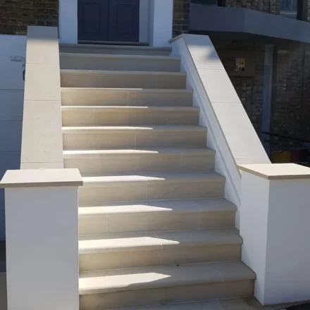 Close-up of renovated residential entrance steps with light stone finish and white rendered side walls