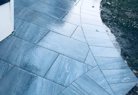 Close-up of grey outdoor patio tiles with a curved tiled edge beside a garden