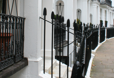 White period townhouses with black iron railings on a residential street in Kensington, London