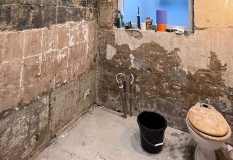 Bathroom refurbishment in progress with stripped walls, exposed plumbing and toilet