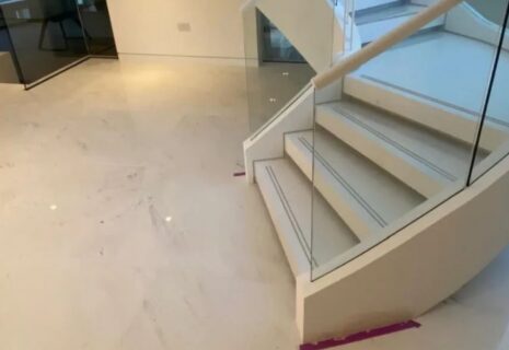 Large-format light floor tiles installed around a curved staircase with glass balustrade