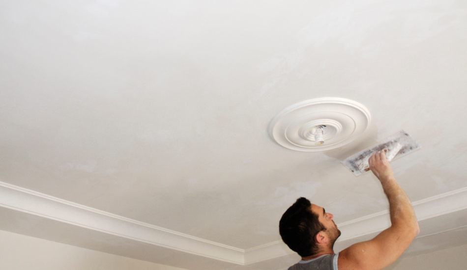 Tradesperson smoothing fresh plaster on an interior ceiling