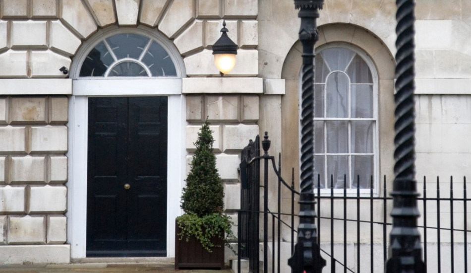 Period stone townhouse entrance with black front door, sash window and iron railings