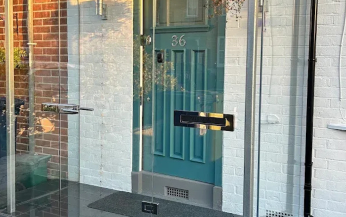 Glass front porch enclosure around a residential entrance with a painted front door