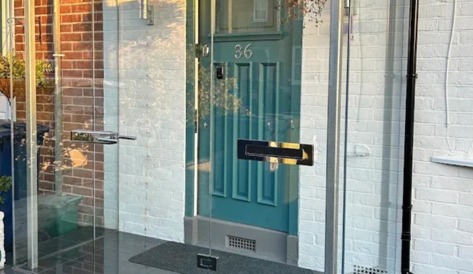 Glass front porch enclosure around a residential entrance with a painted front door