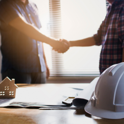 Client and construction professional shaking hands beside building plans and safety helmets