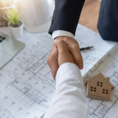 Client and construction professional shaking hands over architectural plans and a model house